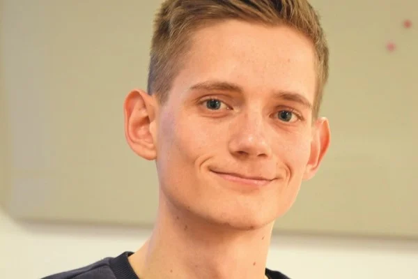 Das Bild zeigt einen jungen Mann der in die Kamera schaut und lächelt