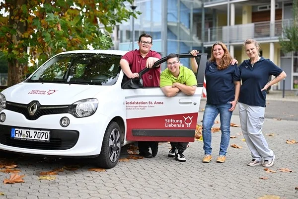 Das Bild zeigt mehrere Personen vor einem offenen Auto