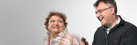 Das Bild zeigt einen Mann, der eine Frau mit einem Stetoskop abhört
