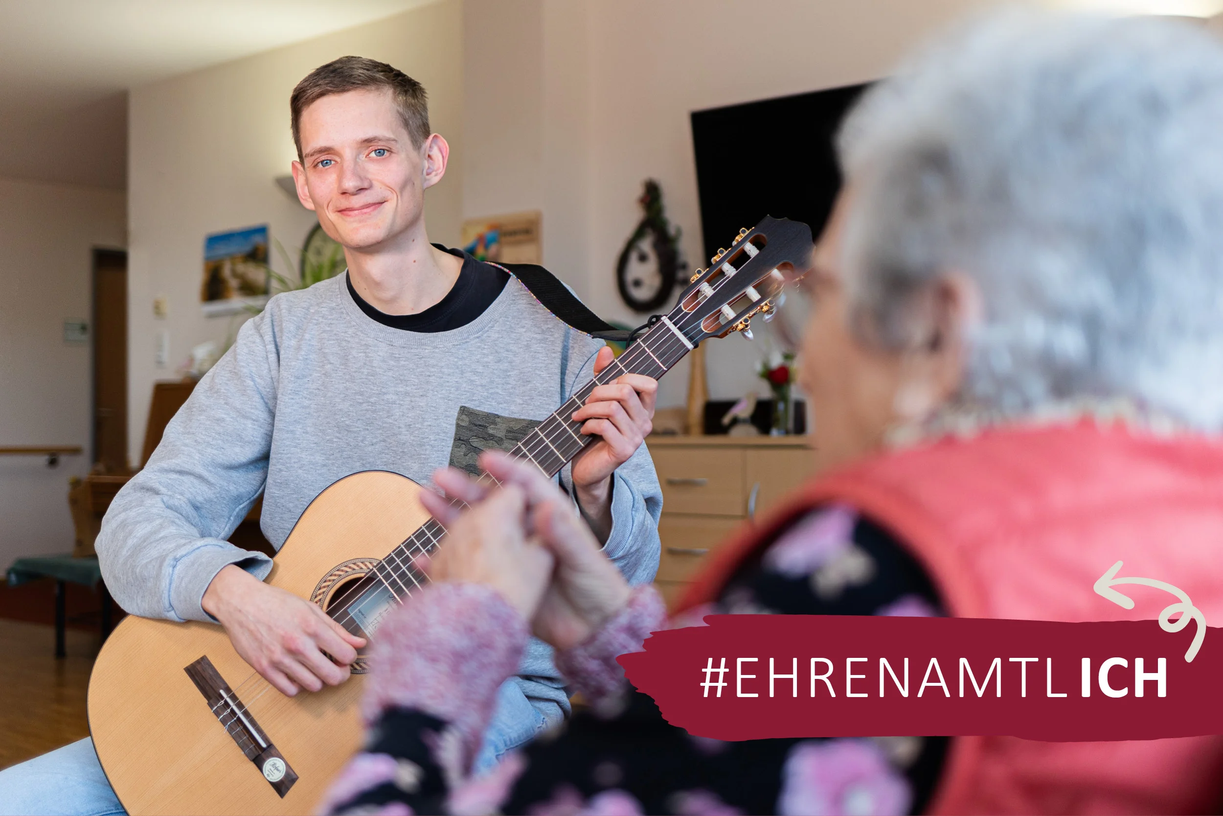 Das Bild zeigt einen jungen Mann der für eine ältere Dame Gitarre spielt.