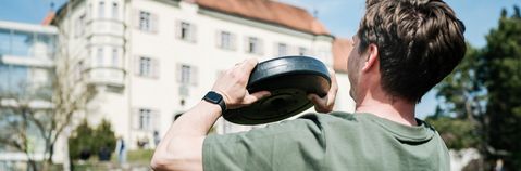 Ein Mann trainiert vor einem großen Gebäude mit einem Gewicht.