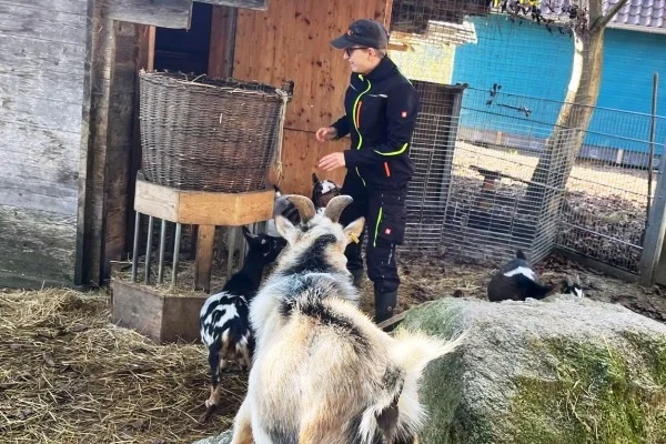 Ein tierisches (Arbeits-) Vergnügen Das Bild zeigt eine jungen Frau mit zwei Ziegen vor einem Stall