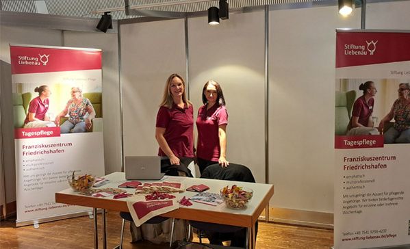 Zwei Frauen stehen in einem Messestand und schauen zur Kamera.