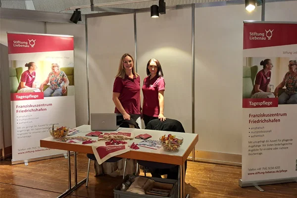 Zwei Frauen stehen in einem Messestand und schauen zur Kamera.