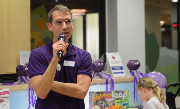 Dr. med. Steffen Kallsen Ein Mann mit Mikrophon spricht, im Hintergrund ist ein spielendes Kind.