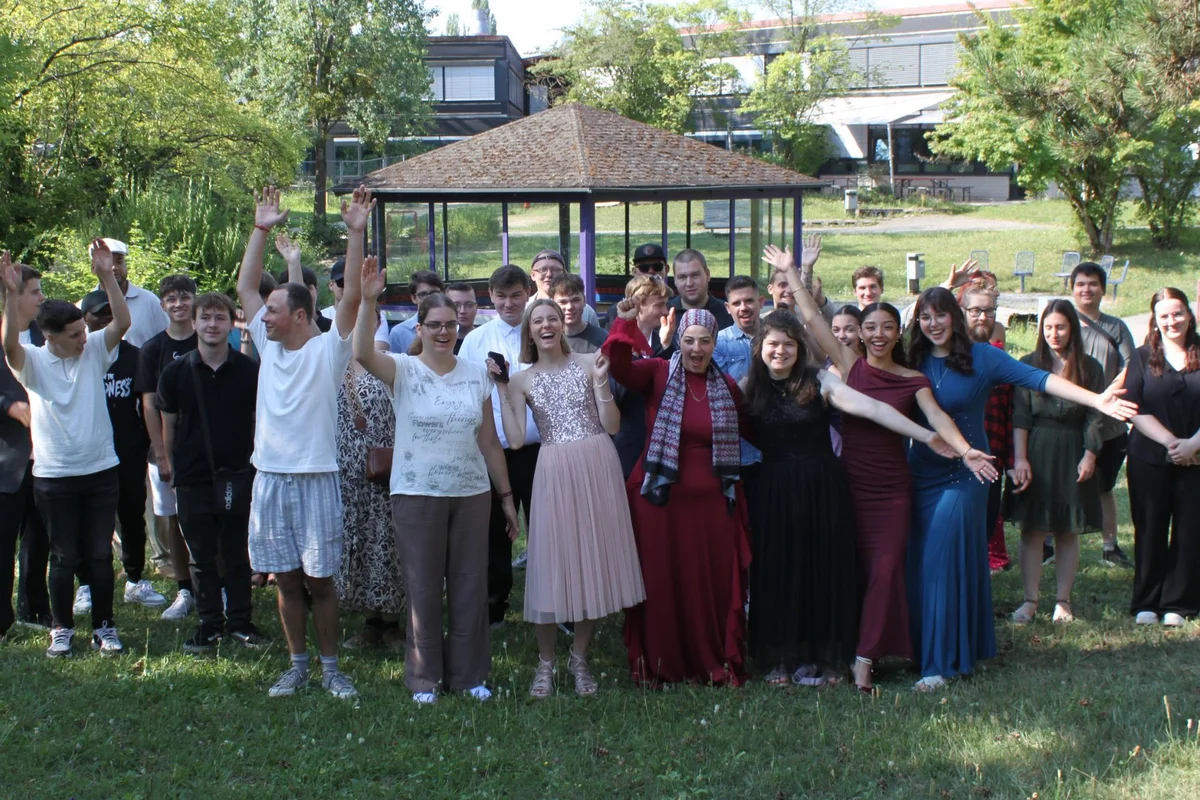 Absolventenfeier Gruppenbild vieler jubelnder Menschen auf einer Wiese.