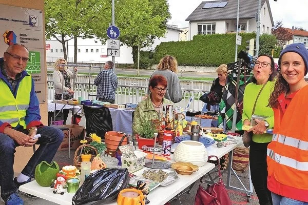 Das Bild zeigt mehrere Personen die gemeinsam an einem Flohmarktstand stehen 