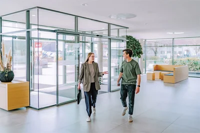 Wie entsteht Haltung? Zwei Personen laufen in einem Foyer in ein Gebäude herein.