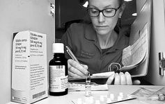 Eine Frau schreibt etwas in einen Ordner und davor liegen Medizinprodukte.