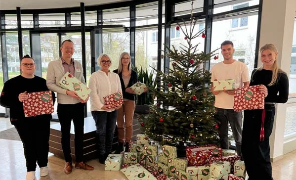 Viele Personen mit Geschenken stehen um einen Christbaum.