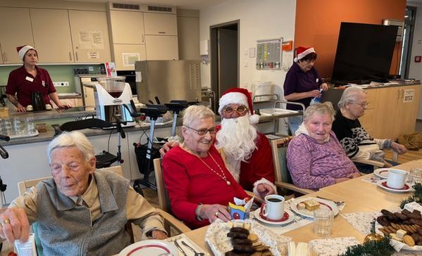 Auf dem Bild sieht man mehrere ältere Menschen die gemeinsam an einem Tisch sitzen und Kuchen essen. Um sie herum stehen Mitarbeitende die als Nikolaus verkleidet sind