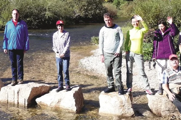 Das Bild zeigt eine gruppe von Personen die auf Steinen in einem Fluss stehen und in die Kamera winken