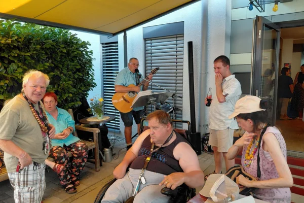 Mehrere Menschen mit Behinderung sitzen zusammen, ein Mann spielt Gitarre und singt.