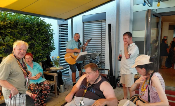 Mehrere Menschen mit Behinderung sitzen zusammen, ein Mann spielt Gitarre und singt.