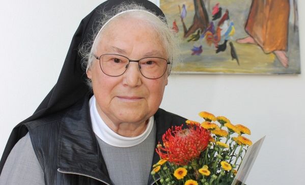 Das Bild zeigt Schwester Willebirg mit Blumenn vor einem Bild des heiligen Franziskus