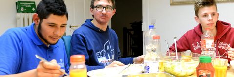 Das Bild zeigt drei junge Männer an einem Tisch beim Essen