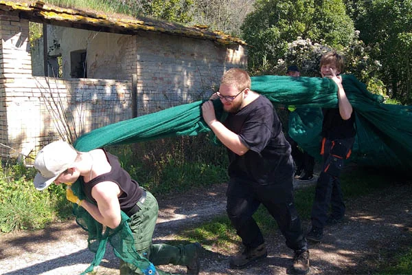 Gartenarbeit und Gemeinschaft bei Franz von Assisi Das Foto zeigt Jugendliche des BBW die ein großes Netz voller Baumschnitt ziehen.
