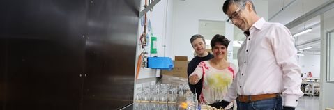 Eine Person arbeitet im Vordergrund und zwei Personen schauen zu.