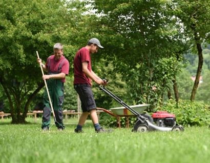 Das Bild zeigt zwei Personen beim Rasen mähen