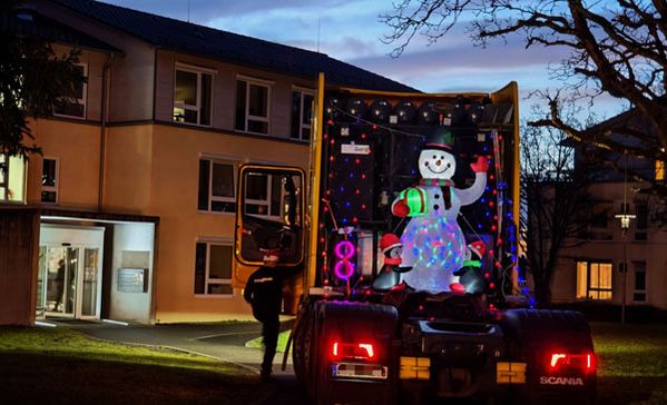 Ein beleuchteter Schneemann im Anhänger eines LKWs vor einem Haus.