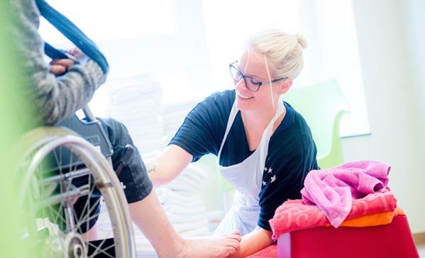 Das Bild zeigt eine Pflegekraft mit einem Pflegebedürftigen im Rollstuhl