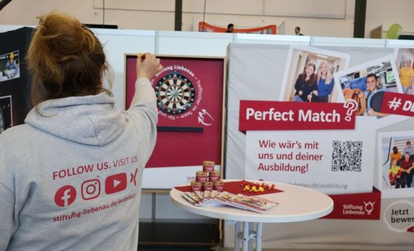 Eine Frau zielt mit einem Dartpfeil auf eine Dartscheibe an einem Messestand.