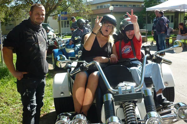 Zwei Personen sitzen auf dem Trike und der Fahrer lächelt in die Kamera.