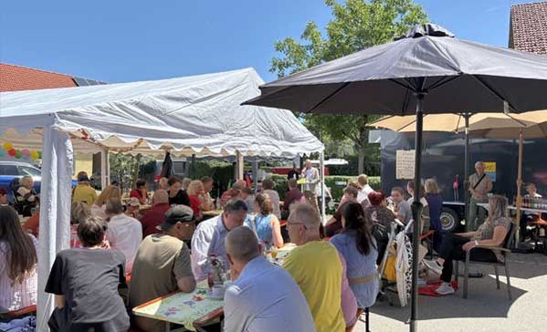 Viele Personen unter Sonnenschirmen bei einem Fest.