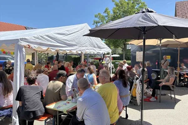 Viele Personen unter Sonnenschirmen bei einem Fest.