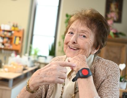 Das Bild zeigt eine ältere Dame in ihrem Wohnzimmer mit einem Notknopfarmband