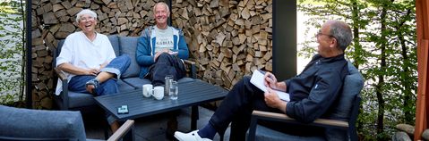 Das Bild zeigt drei Personen im Gespräch auf einer Terasse um einen Tisch sitzend