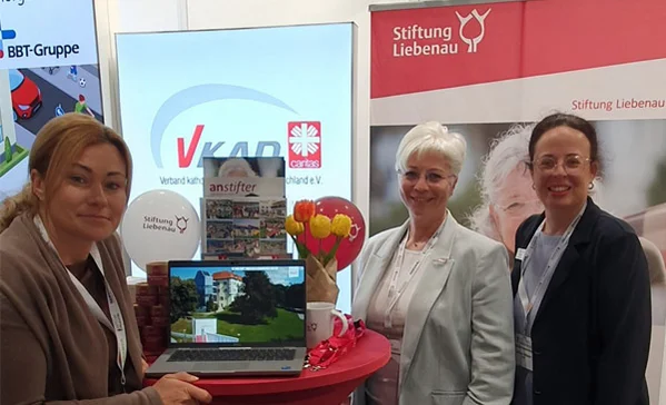 Drei Frauen stehen an einem Messestand und lächeln in die Kamera.