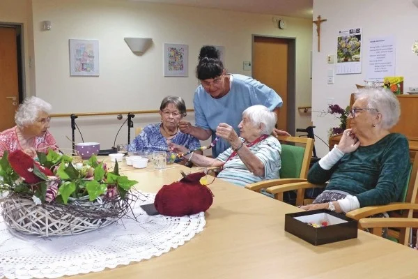 Das Bild zeigt eine Pflegerin die mit vier älteren Personen an einem tisch sitzt und gemeinsam mit ihnen bastelt