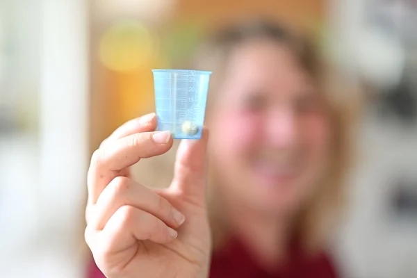 Das Bild zeigt eine Frau mit einem Tablettenbecher in der Hand