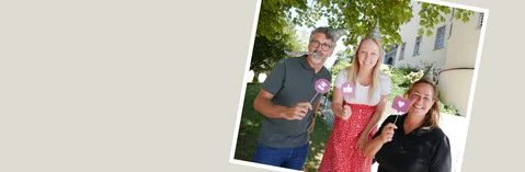 Drei Personen mit Partyhütchen halten kleine Schilder mit Icons hoch und lächeln in die Kamera.