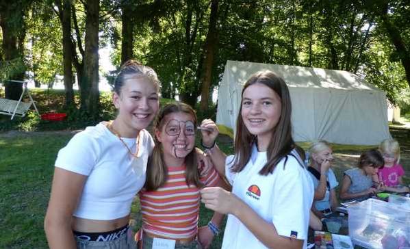 Drei Personen stehen vor einem Zelt und lächeln in die Kamera.