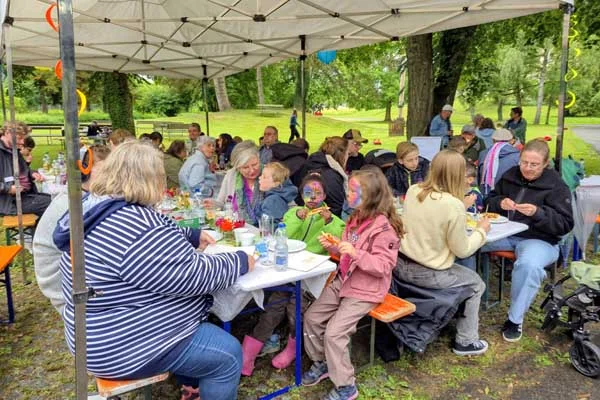 Mehrere Personen sitzen draußen bei einem Fest an Tischen.