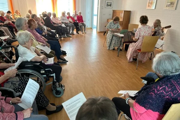 Stubenmusik mit dem Truderinger Saitentrio Das Bild zeigt einen Kreis Zuhörer mit drei Musizierenden