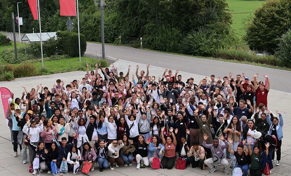 Das Foto zeigt eine große Gruppe winkender, junger Menschen, die mit ihrer Ausbildung beginnen.