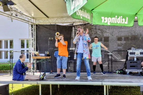 Auf einer Bühne singt ein Mann, während ein anderer Mann Trompete spielt und zwei weitere die Musik genießen.