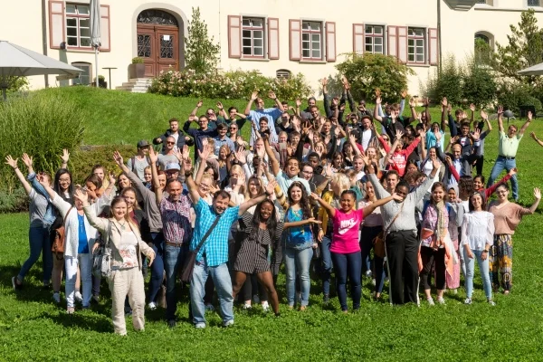 Das Bild zeigt eine Gruppe von Personen die jubelnd ihr Hände in die Luft strecken und in die Kamera lächeln.
