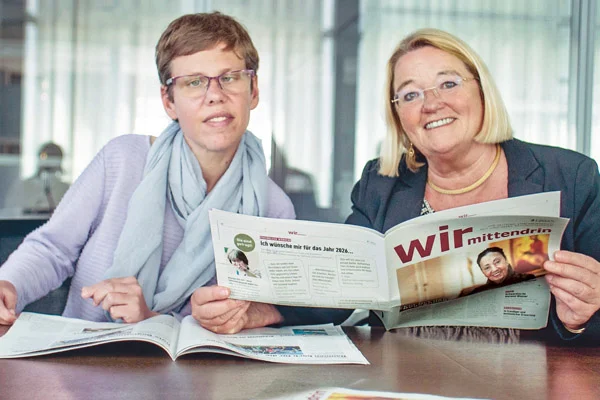 Wir mittendrin Zwei Personen halten eine Zeitung und schauen in die Kamera.