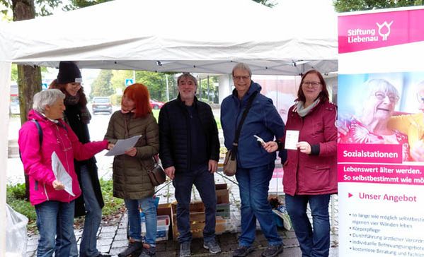 Personen am Marktstand und ein Roll-up der Stiftung Liebenau.