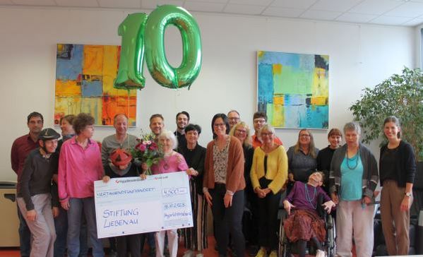 Das Bild zeigt die Übergabe des Spendenschecks durch  Vertreter der HypoVereinsbank an Mitarbeitende und Künstlerinnen und Künstler der Kreativwerkstatt Rosenharz
