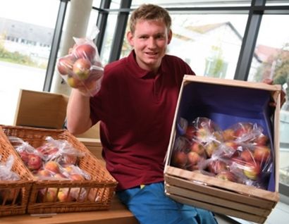 Das Bild zeigt einen jungen Mann mit einem Apfel in der Hand und einer Apfelkiste auf dem Schoß