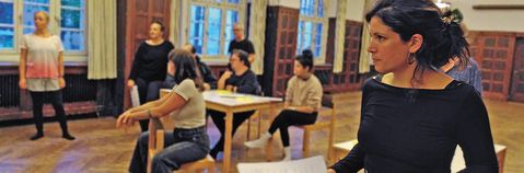 Eine Frau im Vordergrund mit konzentriertem Blick und einige Personen im Hintergrund.