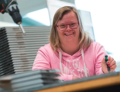 Das Bild zeigt eine junge Frau an einem Tisch in einer Werkstatt