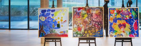 In einer Eingangshalle stehen drei große, bunte Bilder.