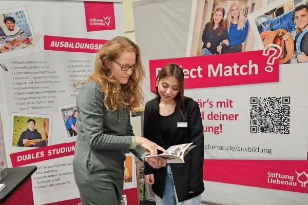 Stiftung Liebenau auf Ulmer Bildungsmesse Das Bild zeigt zwei Frauen im Gespräch vor einer Wand mit Postern
