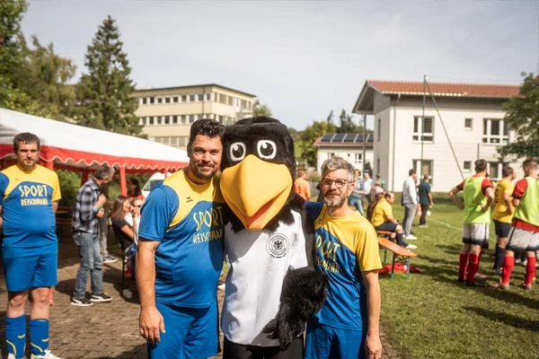 Pokalspiel Zwei Männer und das Maskottchen lächeln in die Kamera